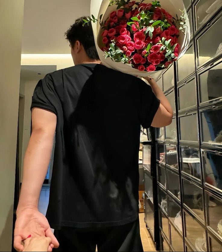A man carrying a large bouquet of red roses, holding her hand.